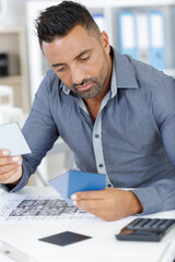 Fototapeta premium architects man working on blueprint plans with calculator and swatches