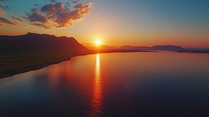 Obraz premium Aerial view of sunset over calm ocean and mountains.
