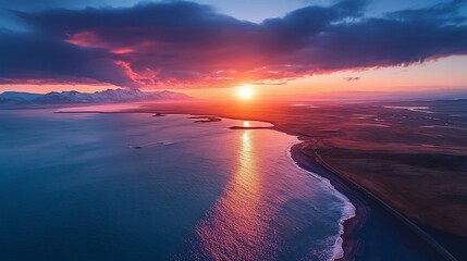Fototapeta premium Vibrant sunset over ocean coast, mountains in distance.