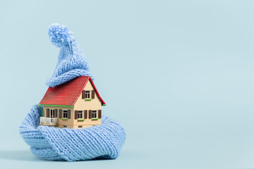 thermal insulation of buildings: old miniature model house with scarf and bobble hat, blue background
