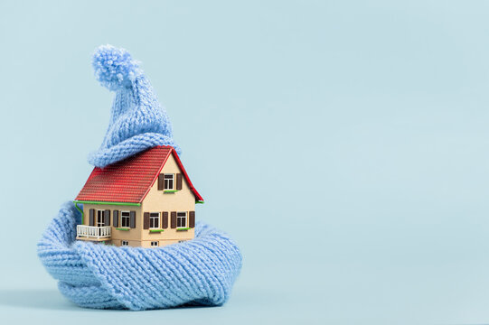 thermal insulation of buildings: old miniature model house with scarf and bobble hat, blue background