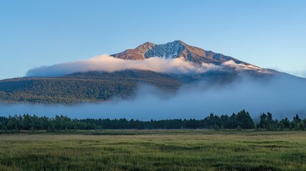 Majestic mountain peak shrouded in clouds illuminated by morning light amidst a serene landscape of lush greenery and mist