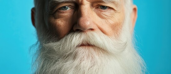 Close up portrait of an elderly man with a thick white beard against a blue backdrop embodying winter holiday spirit and festive cheer