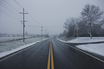 Empty country road with gentle snowfall. Calm weather photograph.