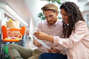 couple doing grocery shopping checking a long receipt