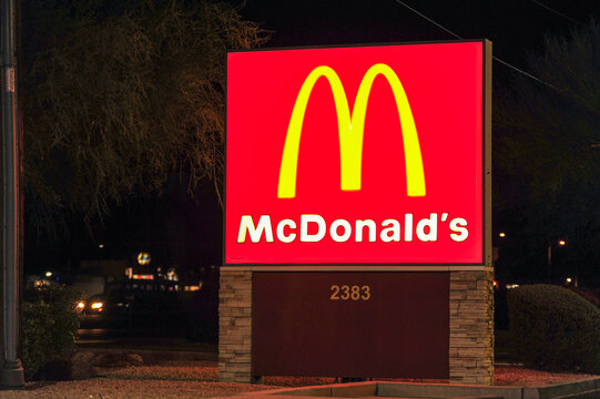 An exterior night view of a McDonald's fast-food restaurant illuminated monument sign, showcasing the iconic brand name and golden arches logo