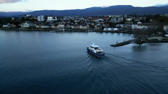 Push in drone shot of boat arriving in Nyon port with cityscape at sunrise in Canton of Vaud Switzerland