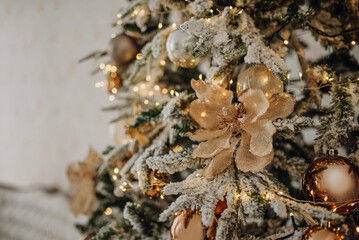 A Christmas tree with snow-covered branches and decor with brown, orange and gold balls, flowers....