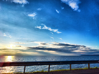 Fototapeta premium A serene sunset over calm waters alongside a tranquil road by the coast, capturing nature's beauty and peacefulness