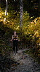 Fototapeta premium A beautiful young hiker woman in a pine forest. Tourist girl with a backpack travelling alone in the nature. Female traveler walk in the autumn fall forest for health. Hiking. Forest mood. Vertical.