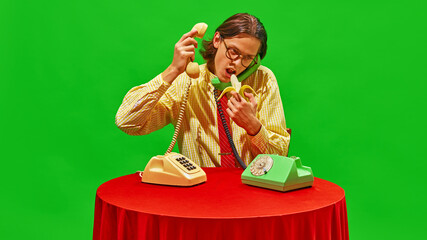 Man stares at banana while talking on two vintage phones, adding quirky and humorous twist to...