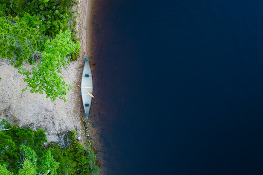Aerial View of Canoe on Sandy Shoreline with Blue Water and Gree