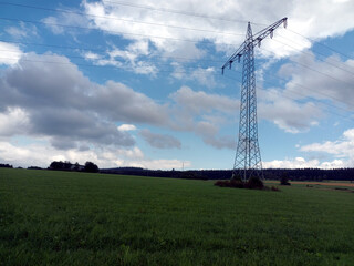 Strommast mit Stromleitungen in der Natur auf einer Wiese mit einem Wald im Hintergrund in der...