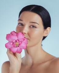 Fototapeta premium A serene young woman gently holds a vibrant pink lotus flower near her face, symbolizing natural beauty and purity. Her flawless skin and calm expression make this image ideal for skincare, beauty