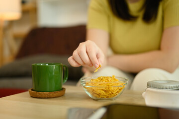 Close up of woman hand picking up a cornflake from a glass bowl