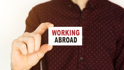 Businessman holding a card with text WORKING ABROAD