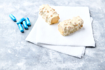 Protein bar in two pieces and amino acids capsules on wooden background. Soft focus. Close up. Copy space
