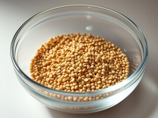 Tiny brown millet grains in a shallow, rounded glass bowl, tiny, small grain, glass
