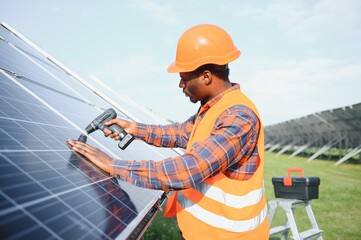 African american man in safety helmet on solar panels with screwdriver. Competent technician using...