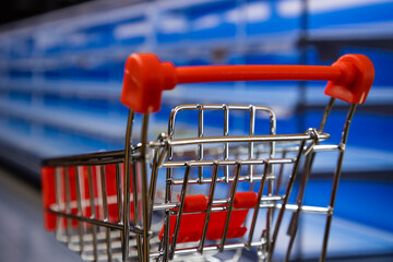 Close up of shopping cart in a supermarket with empty shelves in the background out of focus. Food...
