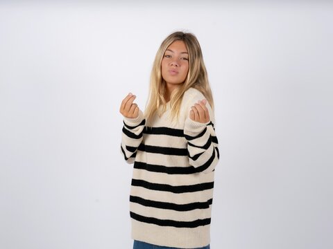 Beautiful teen girl wearing striped sweater doing money gesture with hands, asking for salary payment, millionaire business