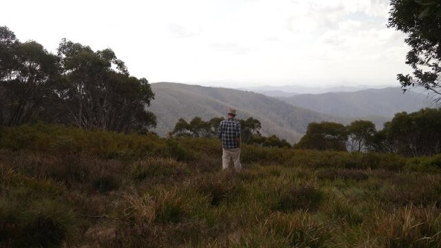 Australian bushman walks towards the edge of a mountain range lookout in the Australian wilderness.