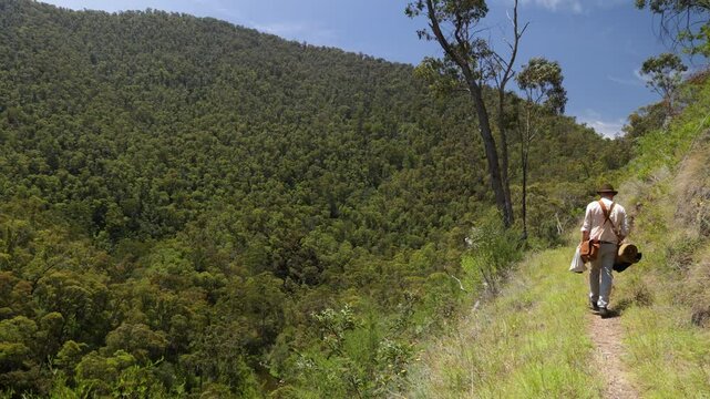 A traditional Australian bushman walks along a wilderness mountain track.