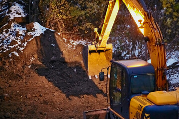 A backhoe loader and the shadow of its bucket on the ground at a construction site in winter, construction work during the off-season, round-the-clock construction work