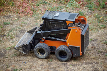 Fototapeta premium Mini loader on an earthen site with dry grass, loader ready to work