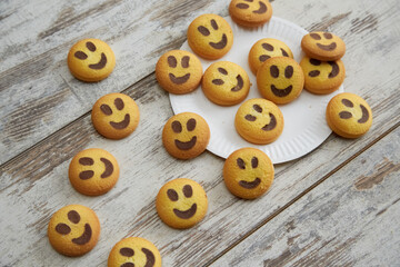 Obraz premium Emoji smiley cookies scattered from a white plate on a wooden table in close-up, good mood, casual communication, good family atmosphere, happiness and joy.