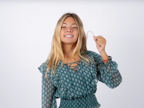 Beautiful teen girl wearing green fashion T-shirt holding an invisible braces aligner, recommending this new treatment. Dental healthcare concept.