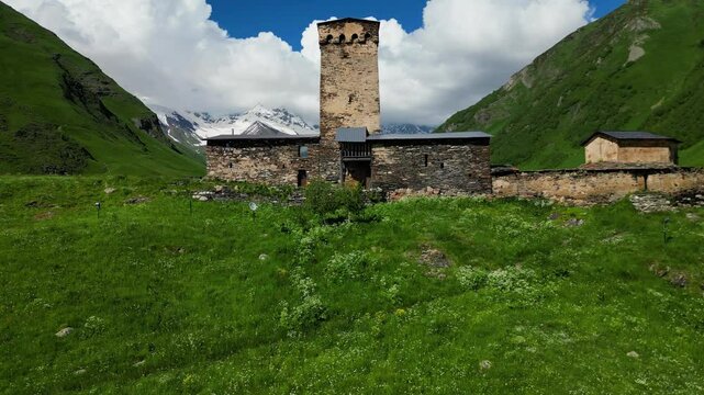 Aerial Drone Footage Captures Lamaria Church In Ushguli, Georgia, Rising Above Wildflowers. Surrounded By Majestic Mountains, This Serene Summer Scene Evokes Tranquility And Beauty.
