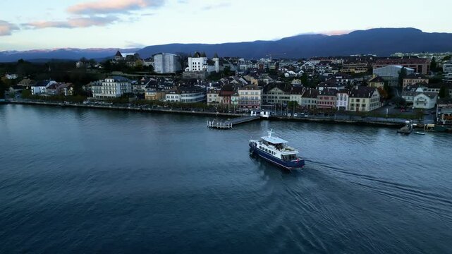 Orbit drone shot of boat arriving in Nyon port at sunrise with cityscape in Canton of Vaud Switzerland