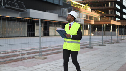 Architect walking and inspecting a building construction site holding blueprints