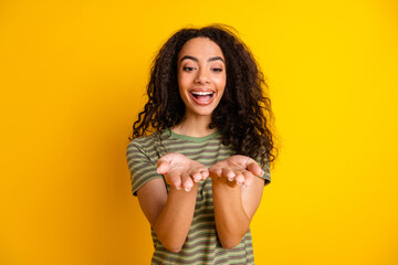 Photo of impressed overjoyed girl with wavy hairstyle dressed striped t-shirt look at object on palms isolated on yellow color background