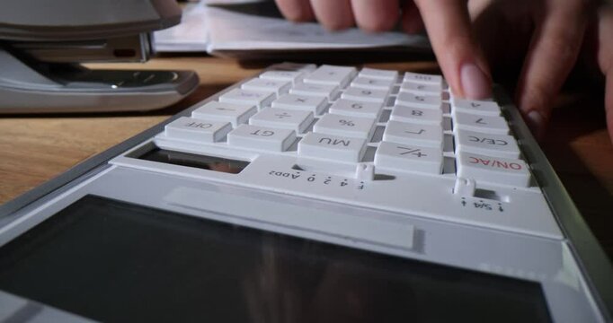 Woman presses buttons on calculator working at table in office. Female accountant calculates payroll amounts in professional environment