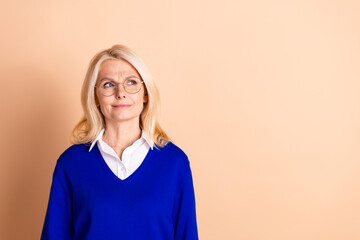 Confident mature woman in blue pullover against beige background exuding elegance and professional competence