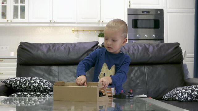 Impatient child unboxing new toy at home. Excited little boy unpacks remote-controlled transformer car.