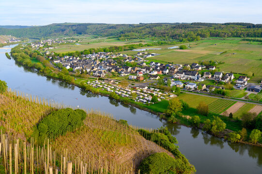 Aerial view of Mosel river landscape with the small villages Erden and Loesnich, surrounded by lush greenery, vineyards and fields. A camping park with caravans and RV's is at the bank. 