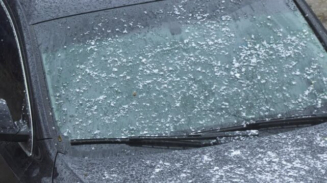 Wet snow falls on windshield of car parked on street.