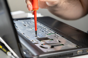 hand using a screwdriver to adjust a component inside a laptop during repair, focusing on the...