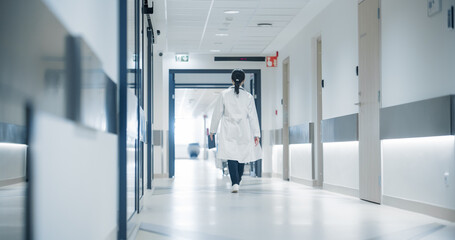 Female Doctor Walking Away in an Empty Hospital Hallway. General Practitioner Holding a Tablet...