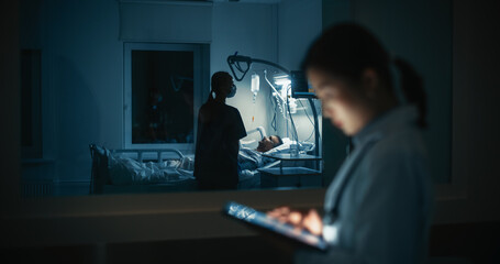 Outside a Dimly Lit Hospital Room, Young Asian Female Doctor Using a Tablet Computer, Analyzing...
