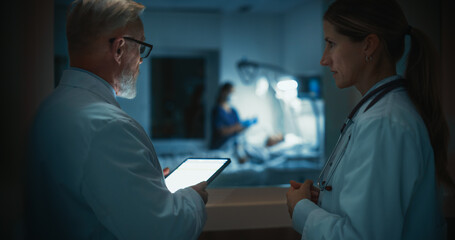 Obraz premium Senior Doctor Holding a Tablet Computer, Sharing Critical Patient Data With a Female Colleague Outside a Hospital Ward with Nurse and Patient, Their Discussion Focused on Treatment Strategies