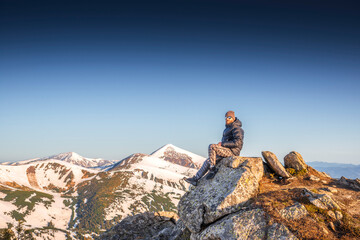 Stylish man with a beard and curled mustache enjoying view from top of a rocky mountain at sunrise...