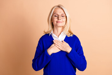 Elegant senior woman with blond hair in blue jumper relaxing against beige background