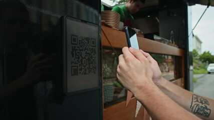 Cropped shot of hands of unrecognizable customer pointing mobile phone camera on QR code to pay for food in street cafe van
