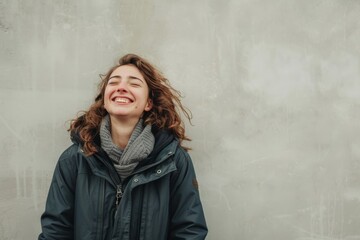 Obraz premium Portrait of a joyful caucasian woman in her 30s wearing a lightweight packable anorak while standing against bare concrete or plaster wall
