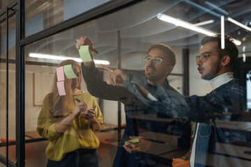 Business team brainstorming and planning using sticky notes on glass wall in office