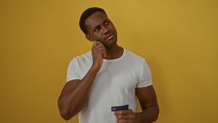 Young man in white shirt holding a credit card against an isolated yellow background, exhibiting...